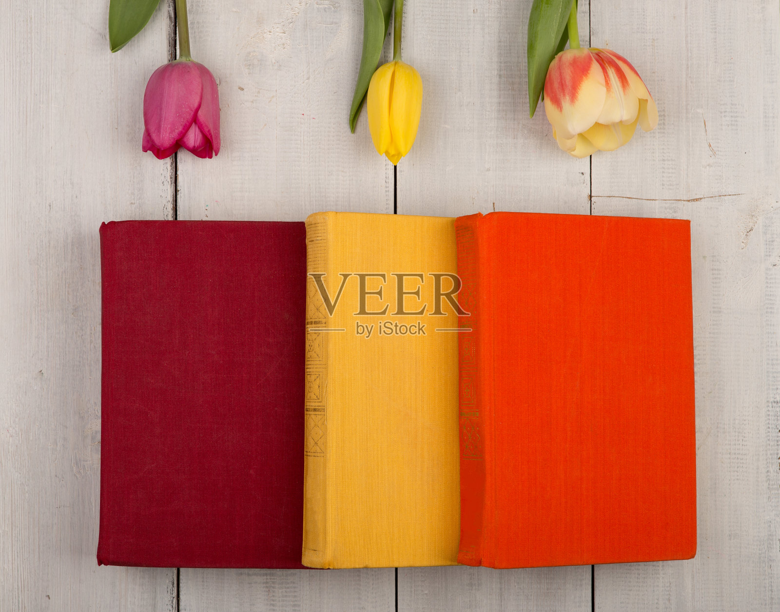 白色的木桌上放着鲜花、郁金香和彩色的书照片摄影图片