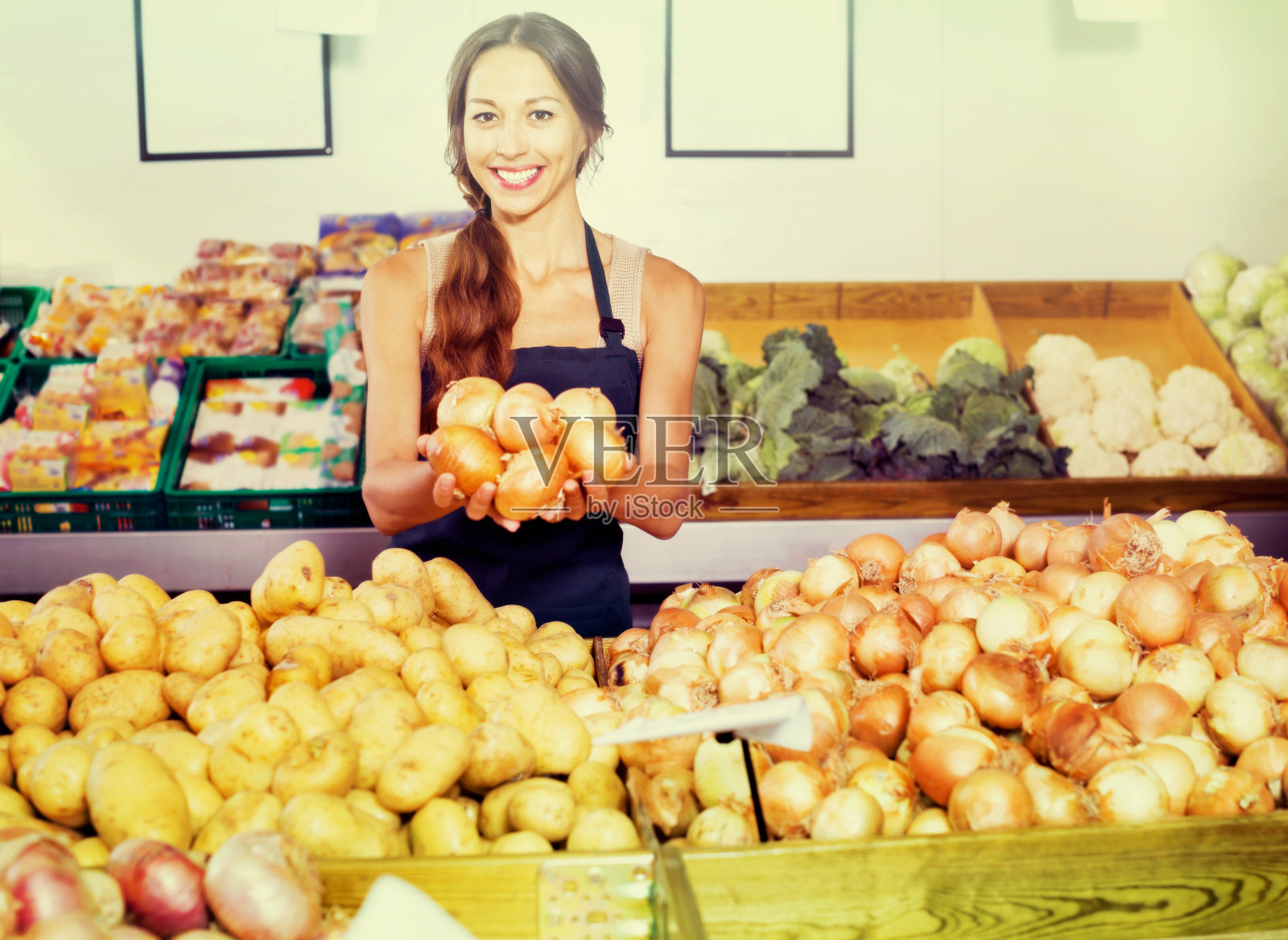 微笑的年轻女子售货员展示黄色的洋葱照片摄影图片