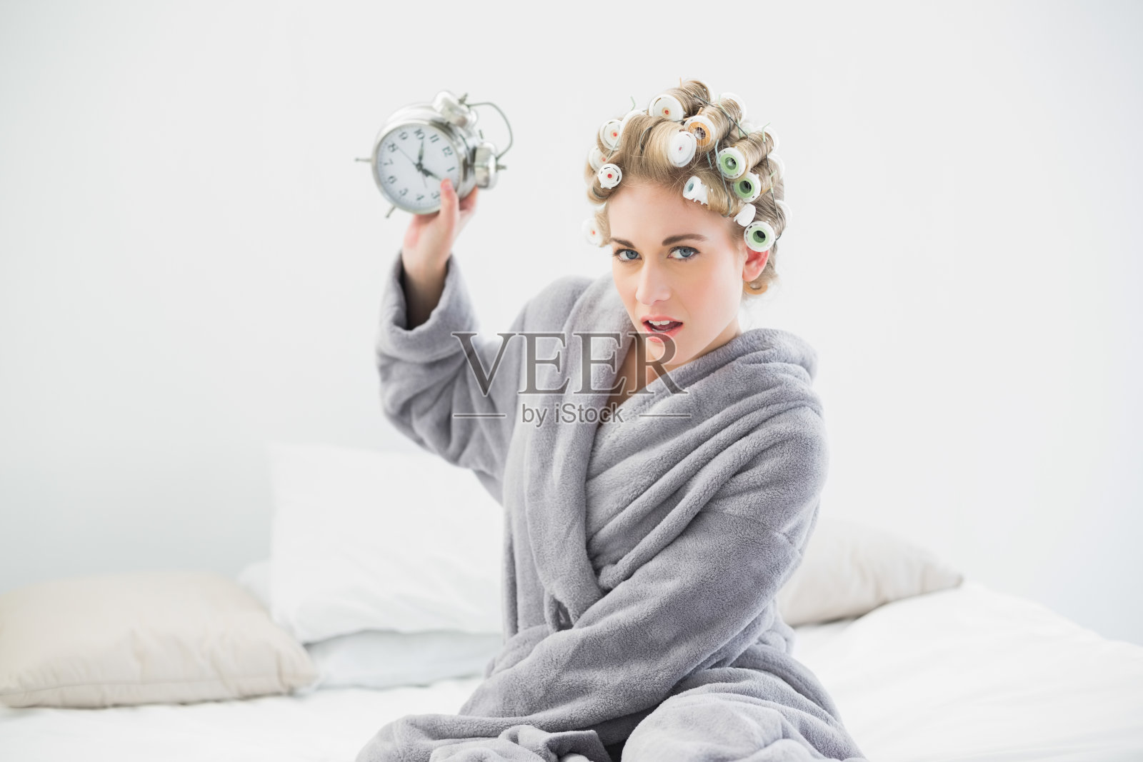 愤怒的金发女人拿着卷发器扔闹钟照片摄影图片
