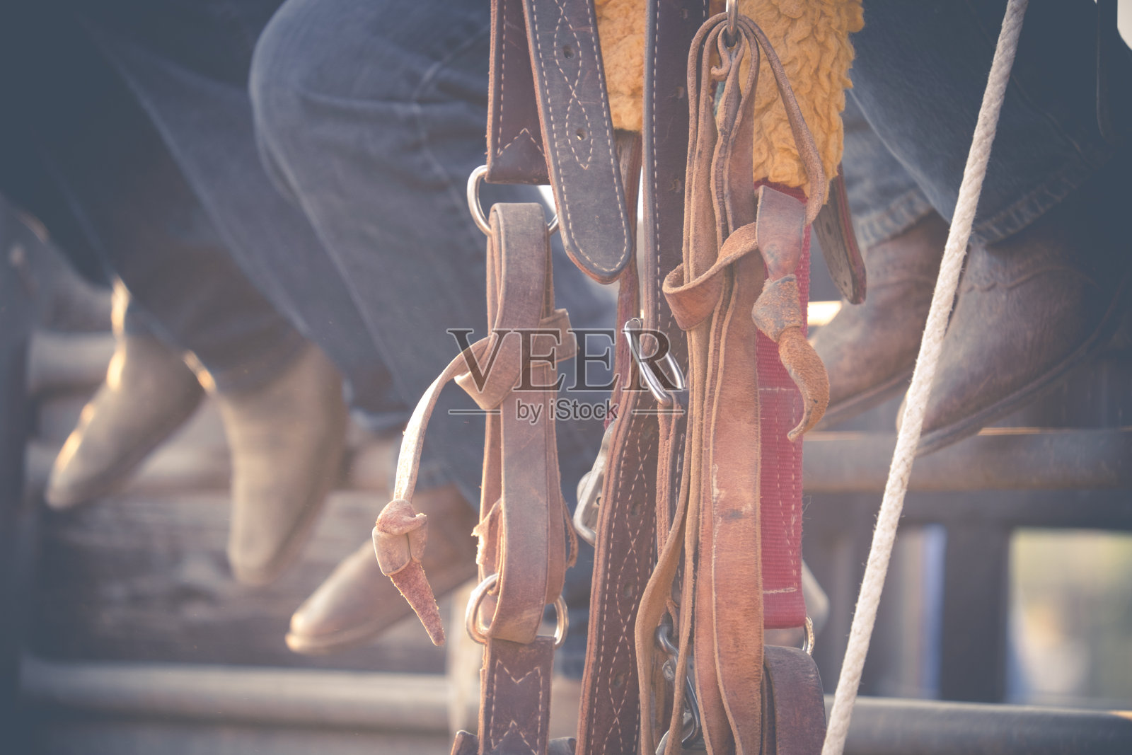 近距离观察三个牛仔坐在珊瑚围栏上，露出他们的靴子，缰绳挂在他们的前面。照片摄影图片