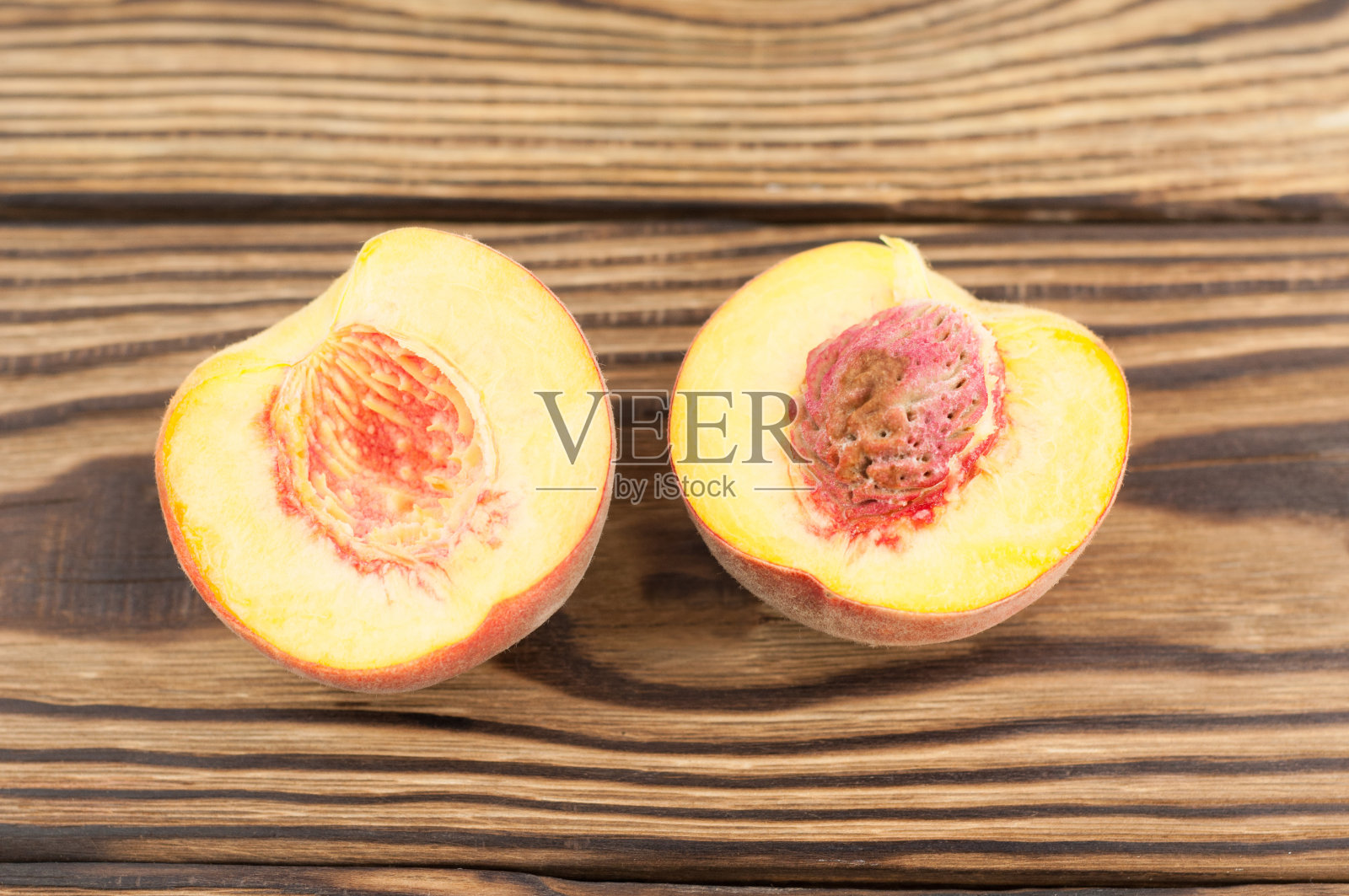 两个半熟的新鲜桃子，上面有桃核，放在粗糙的旧木板上照片摄影图片