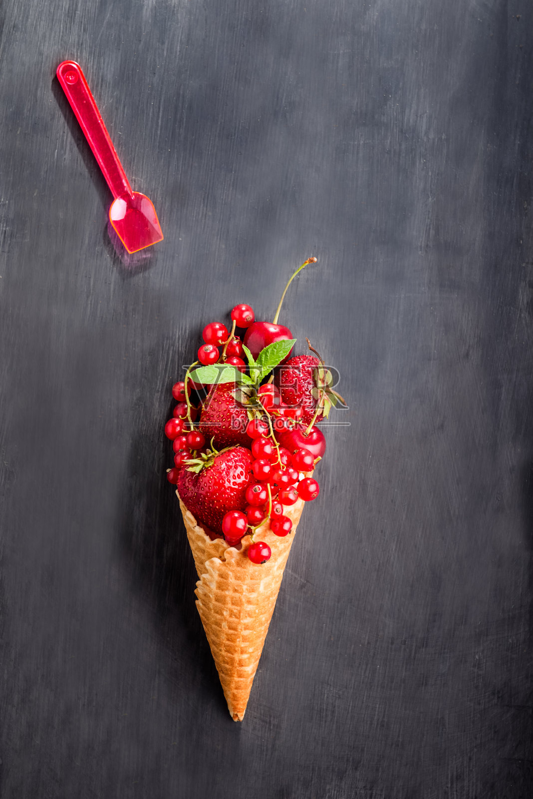 新鲜的夏季红色浆果——草莓、红醋栗、华夫筒冰淇淋中的樱桃和黑色木质背景上的小勺子。健康的甜点。前视图。空间的文本。照片摄影图片