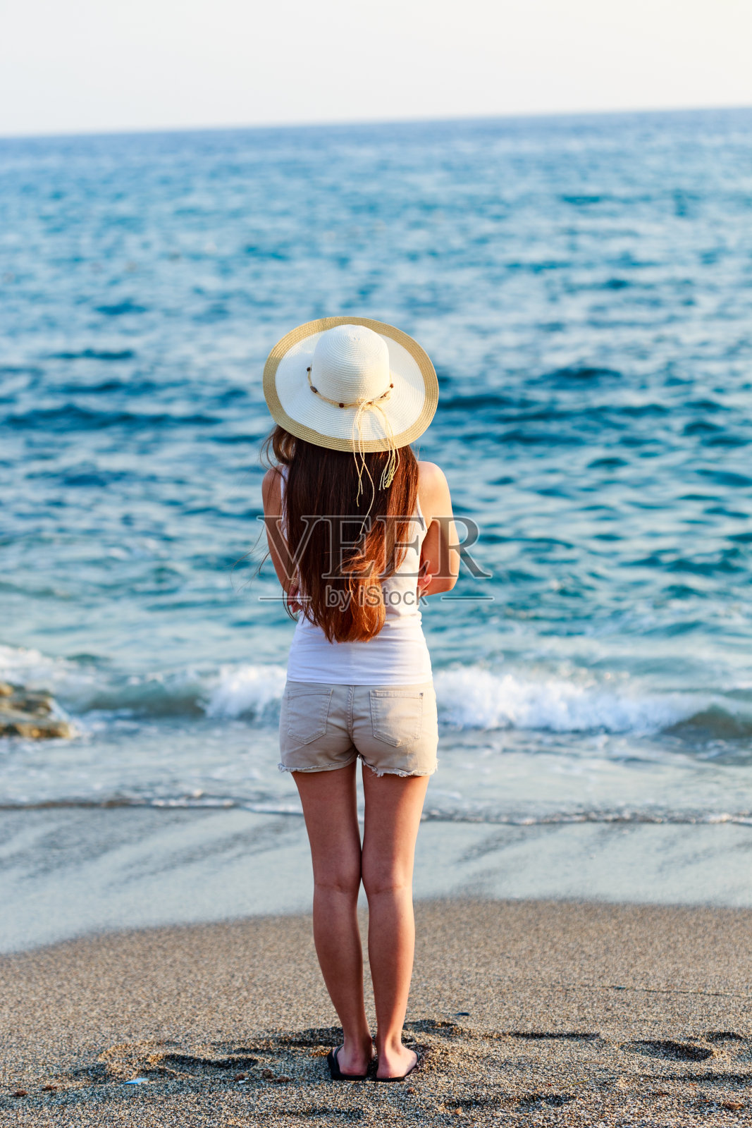 年轻女子在海边穿着夏装，戴着帽子照片摄影图片