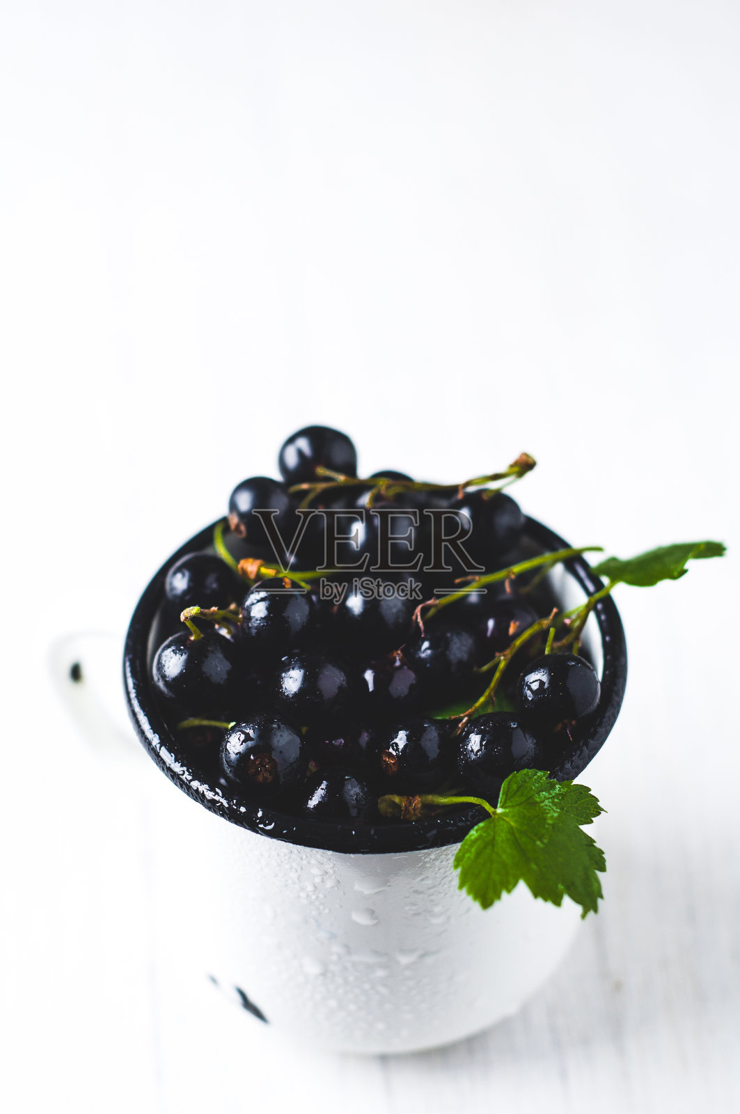 白木色背景上的白色金属杯中的黑醋栗照片摄影图片