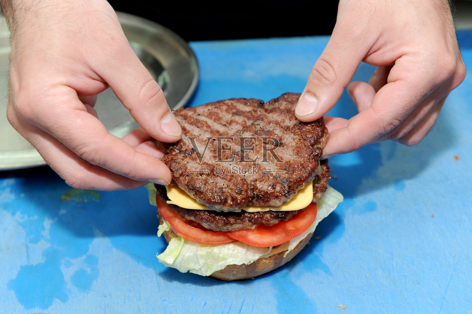 厨师在准备好的汉堡面包上添加汉堡。在厨房里准备和做汉堡包。照片摄影图片