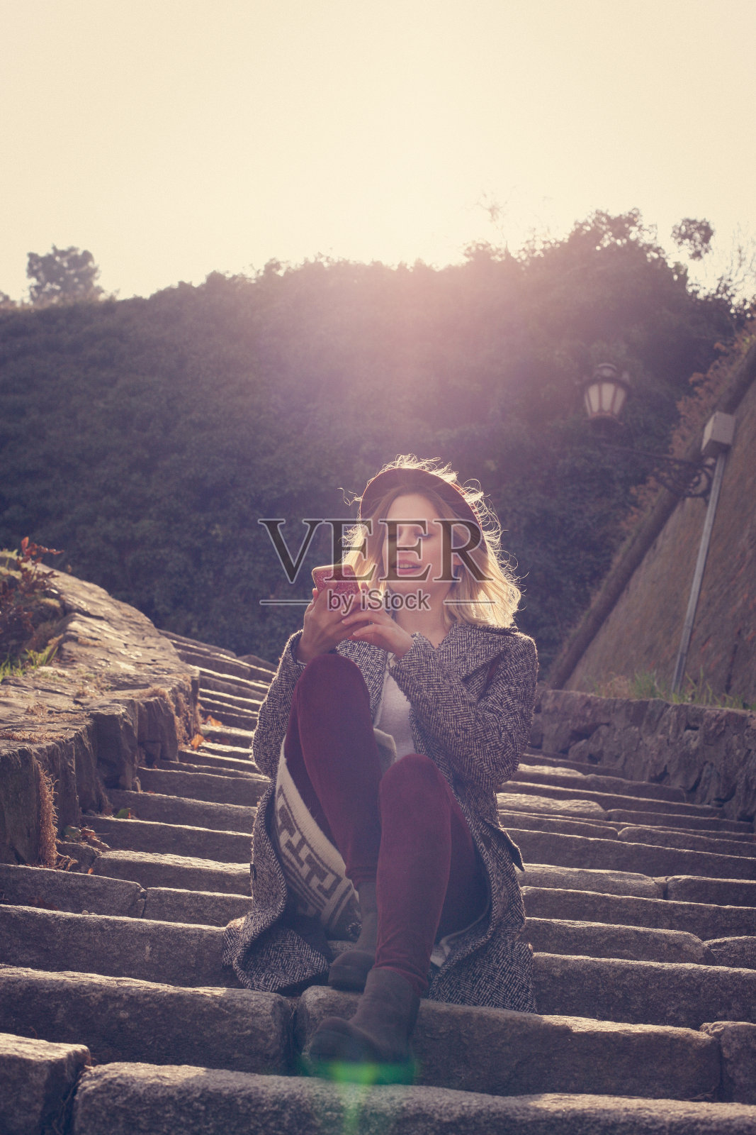 年轻漂亮的女孩坐在公园的楼梯上。年轻漂亮的女孩坐在公园的楼梯上用智能手机。照片摄影图片