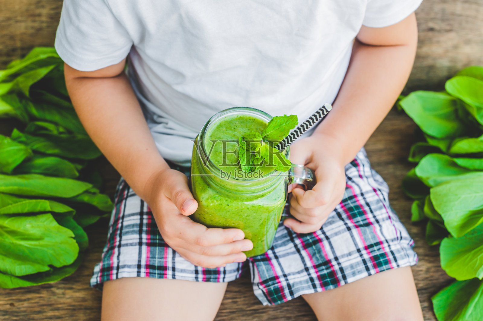 盛满绿色菠菜，香蕉和椰子汁的健康奶昔和一勺燕麦片的玻璃瓶放在木桌上照片摄影图片