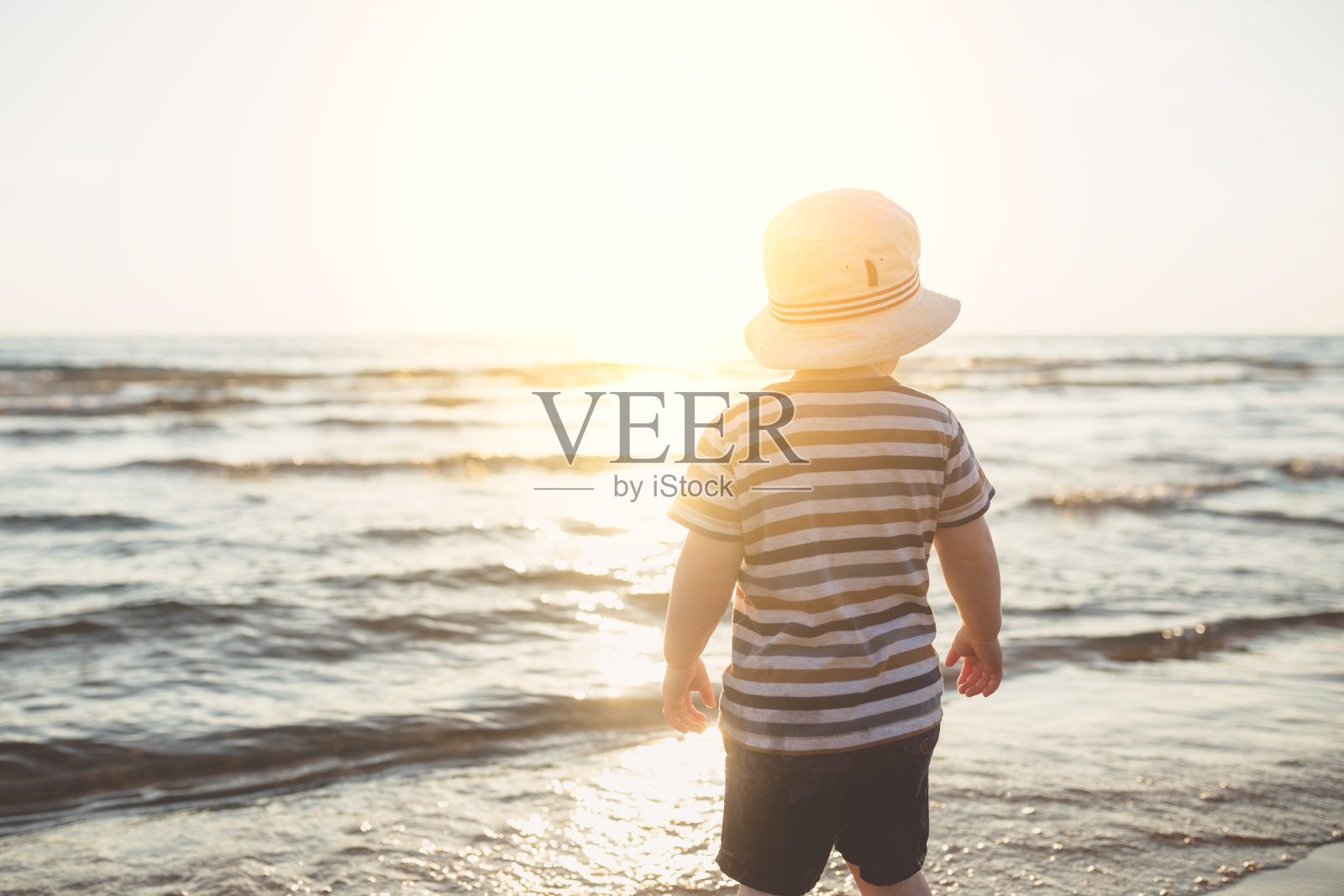 夕阳西下，小男孩站在海边照片摄影图片