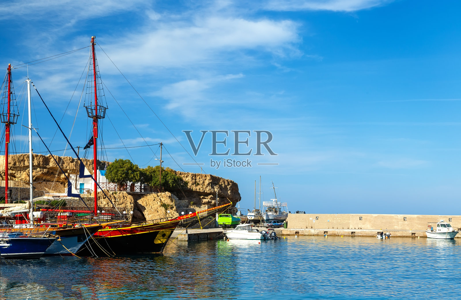 希腊克里特岛的赫尔松索斯港，碧水中的船只和背景上的山丘照片摄影图片