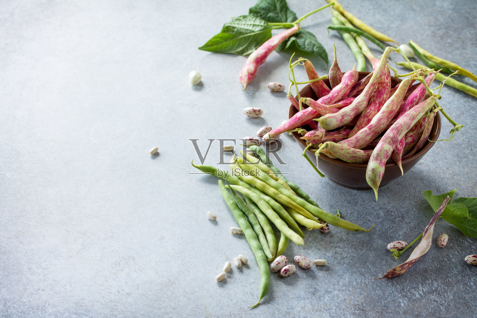 什锦豆荚和豆子。红色和绿色的豆子在灰色的石板或石头的背景上。照片摄影图片
