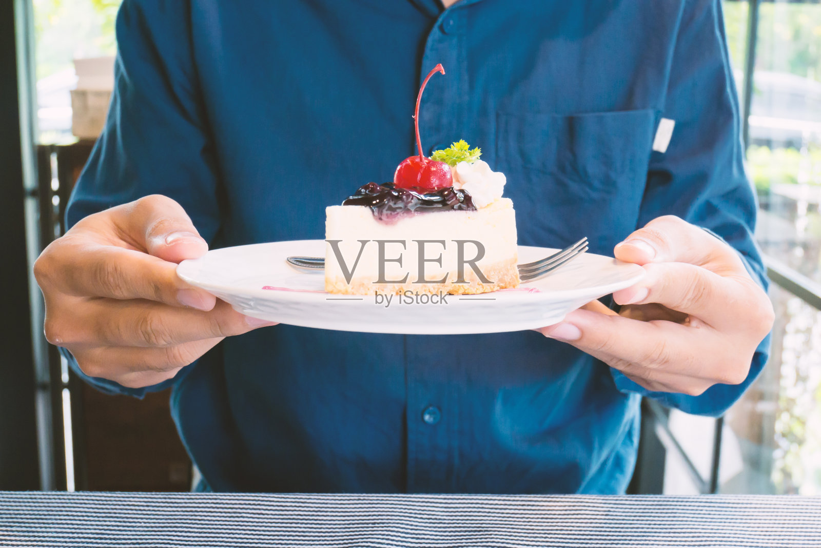 蓝莓芝士蛋糕放在盘子里，用手拿着照片摄影图片