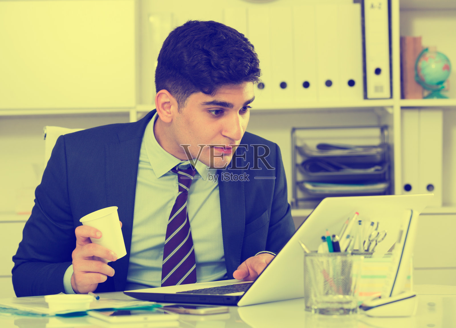 年轻人在电脑前工作，喝着咖啡照片摄影图片