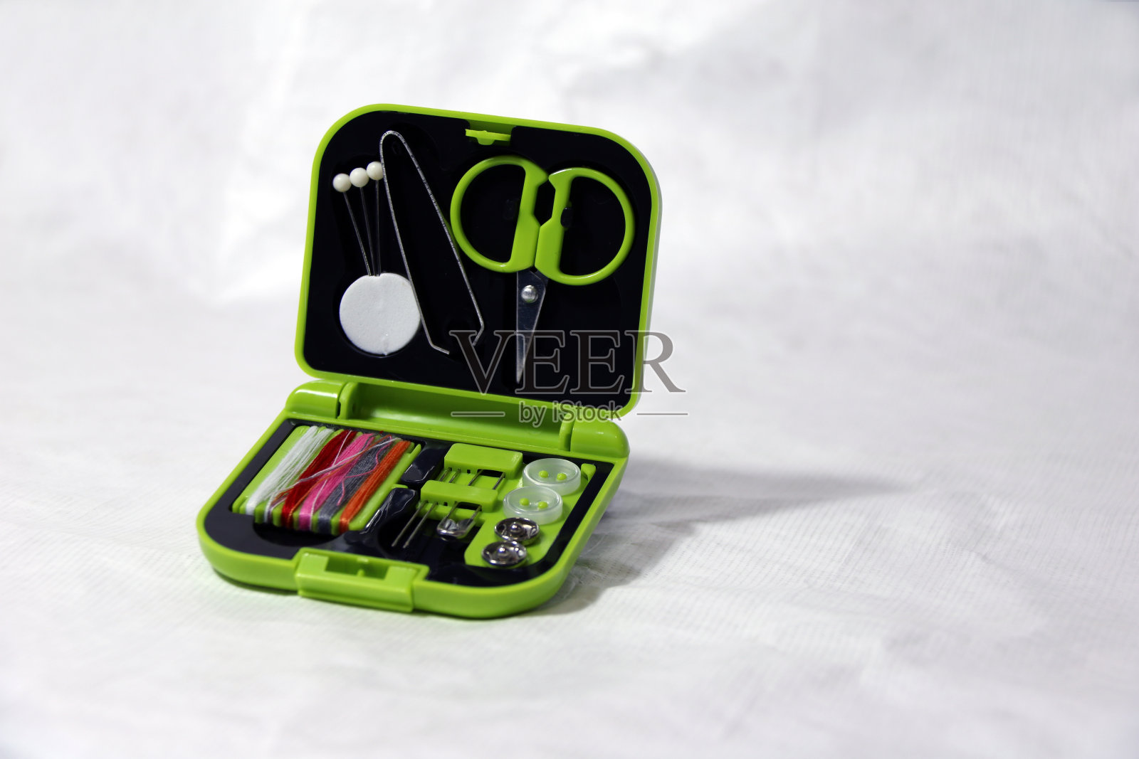 服装修理套装、剪刀、钳子、大头针、缝线针、纽扣和别针在绿色小接线盒中。照片摄影图片