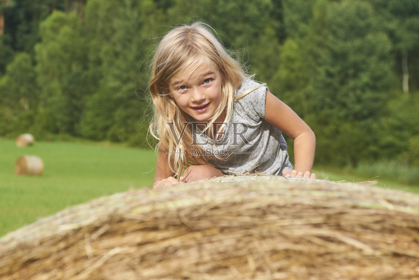 金发碧眼的小女孩在田野里的稻草捆旁。照片摄影图片