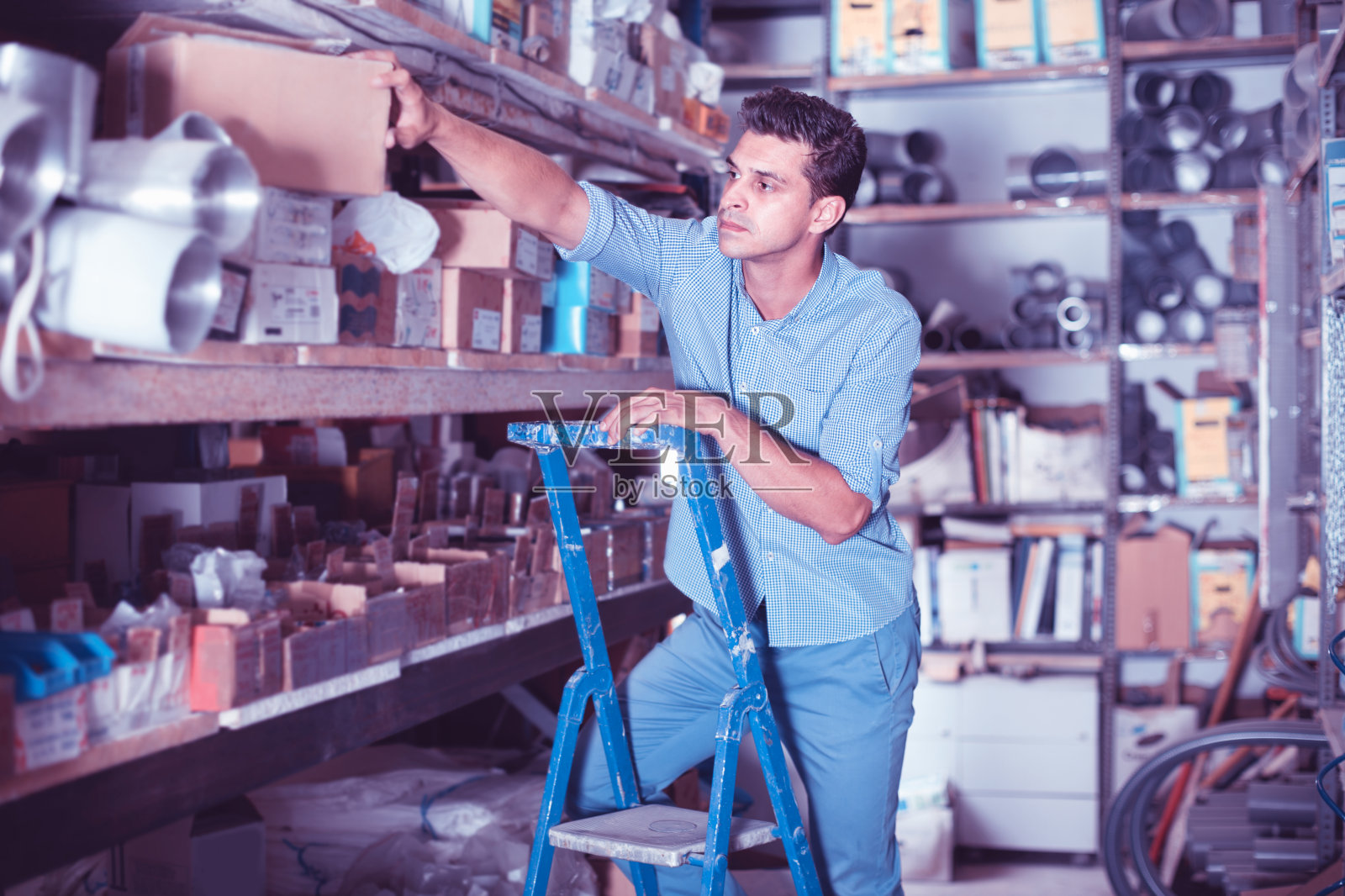 穿制服的人正在用梯子爬到大楼商店的最上面的架子上。照片摄影图片