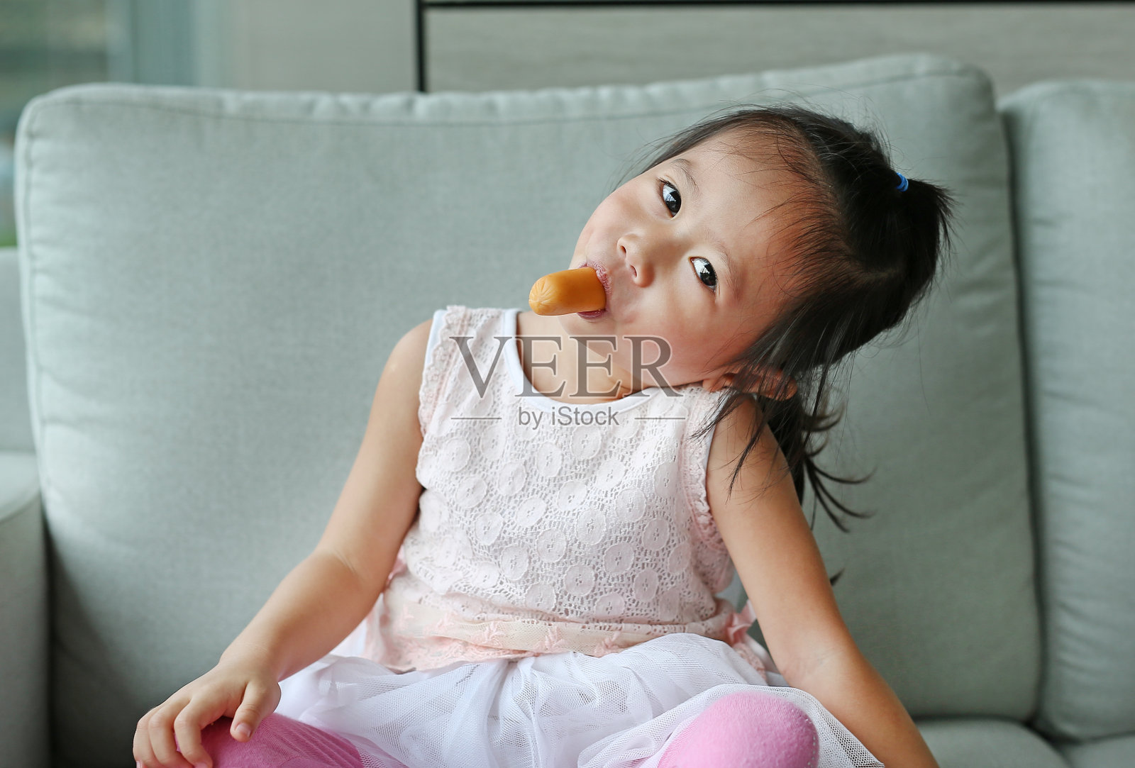 小女孩在沙发上吃香肠。照片摄影图片