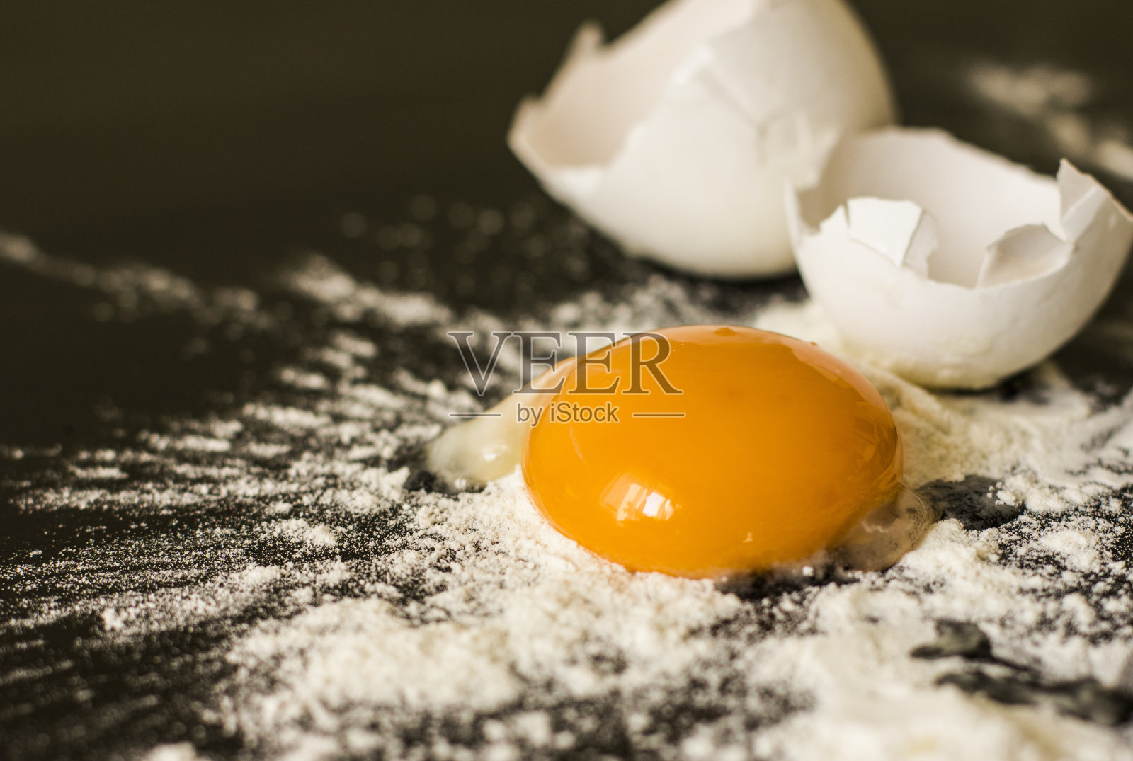 打碎的鸡蛋和面粉放在黑色的桌子上照片摄影图片