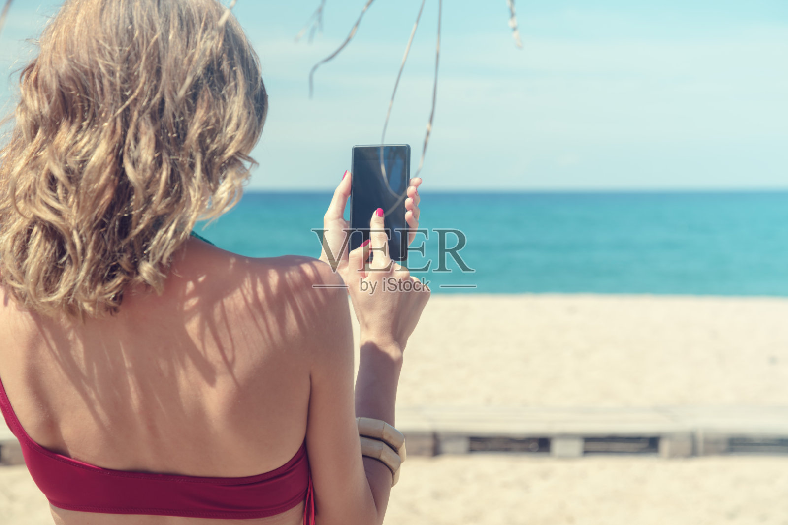 一个年轻女人在沙滩上玩手机。照片摄影图片