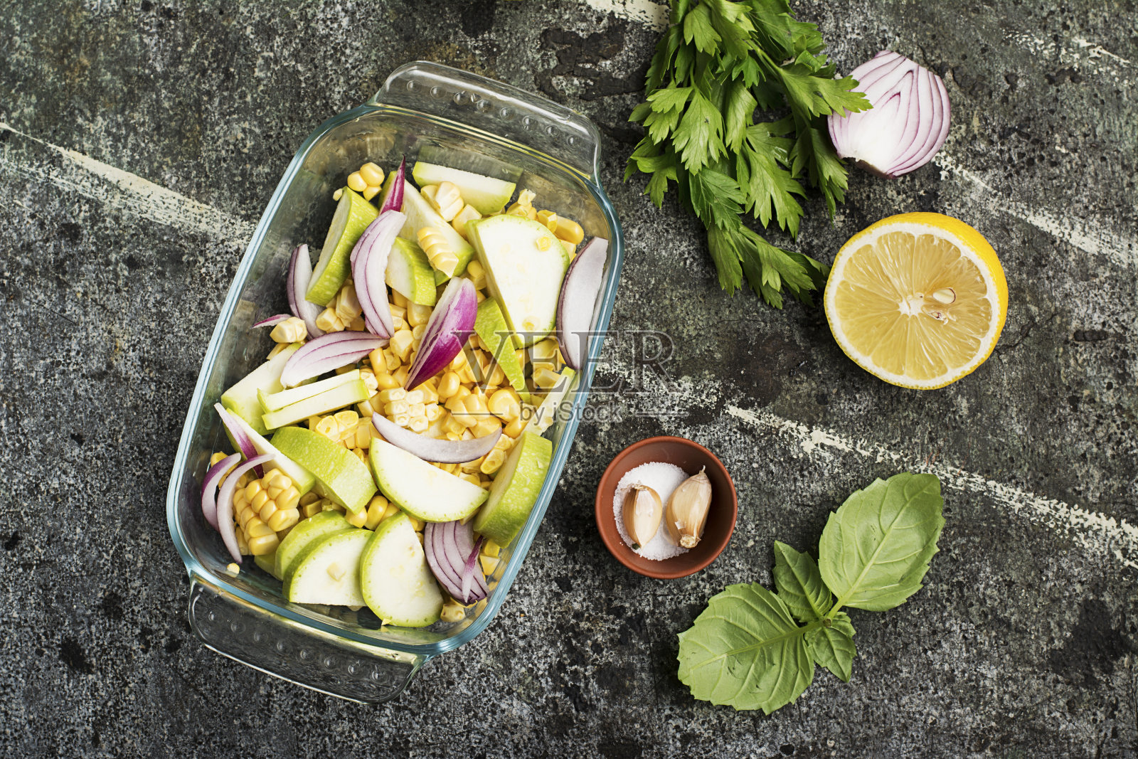 俯视图的蔬菜砂锅，新鲜的时令蔬菜花椰菜，玉米，西葫芦，红色洋葱在一个透明的形式为午餐烘烤。照片摄影图片