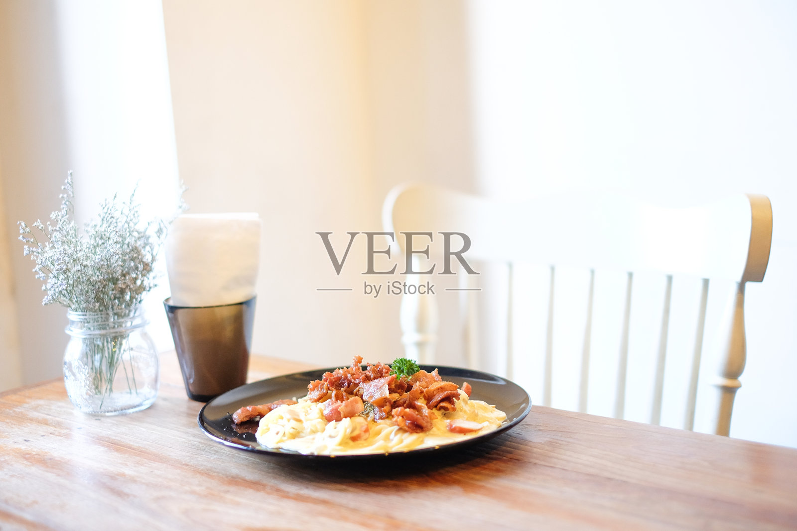 美丽的室内植物放在透明的花盆里，纸巾放在黑色的盒子里，烤意面与培根和蘑菇酱放在木桌和白色椅子上，食物背景或纹理内饰概念。照片摄影图片