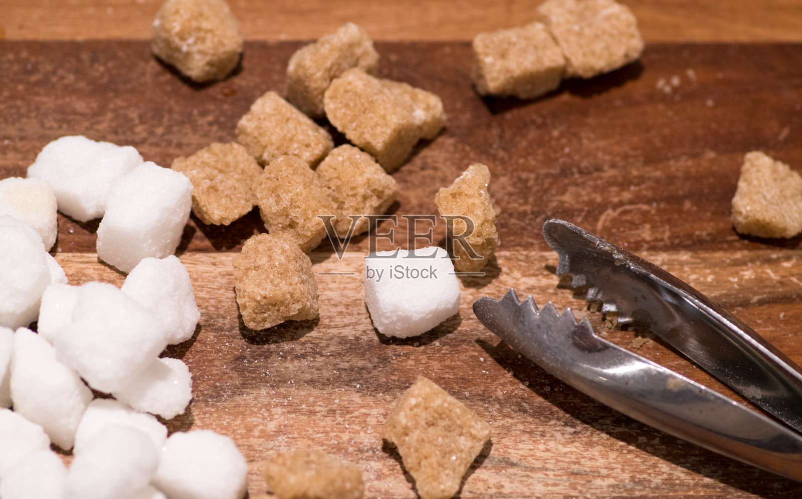 木桌上放着棕色的甘蔗和白色的方糖。特写镜头照片摄影图片
