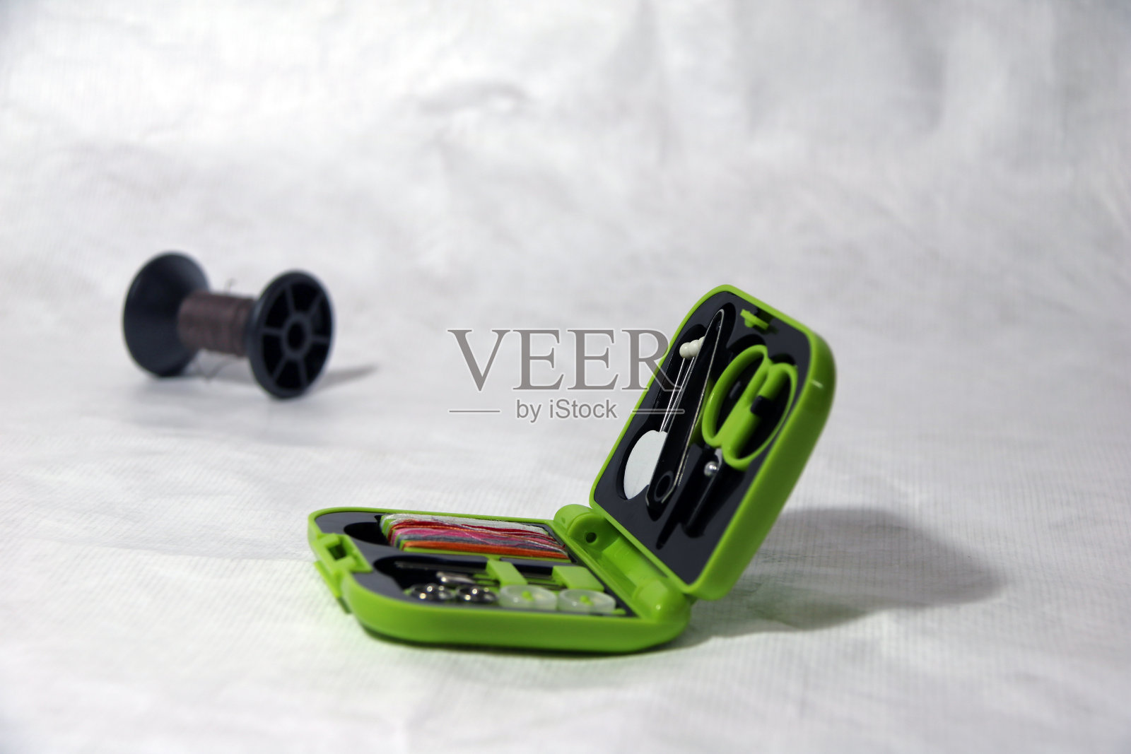 服装修理套装、剪刀、钳子、大头针、缝线针、纽扣和别针在绿色小接线盒中。照片摄影图片