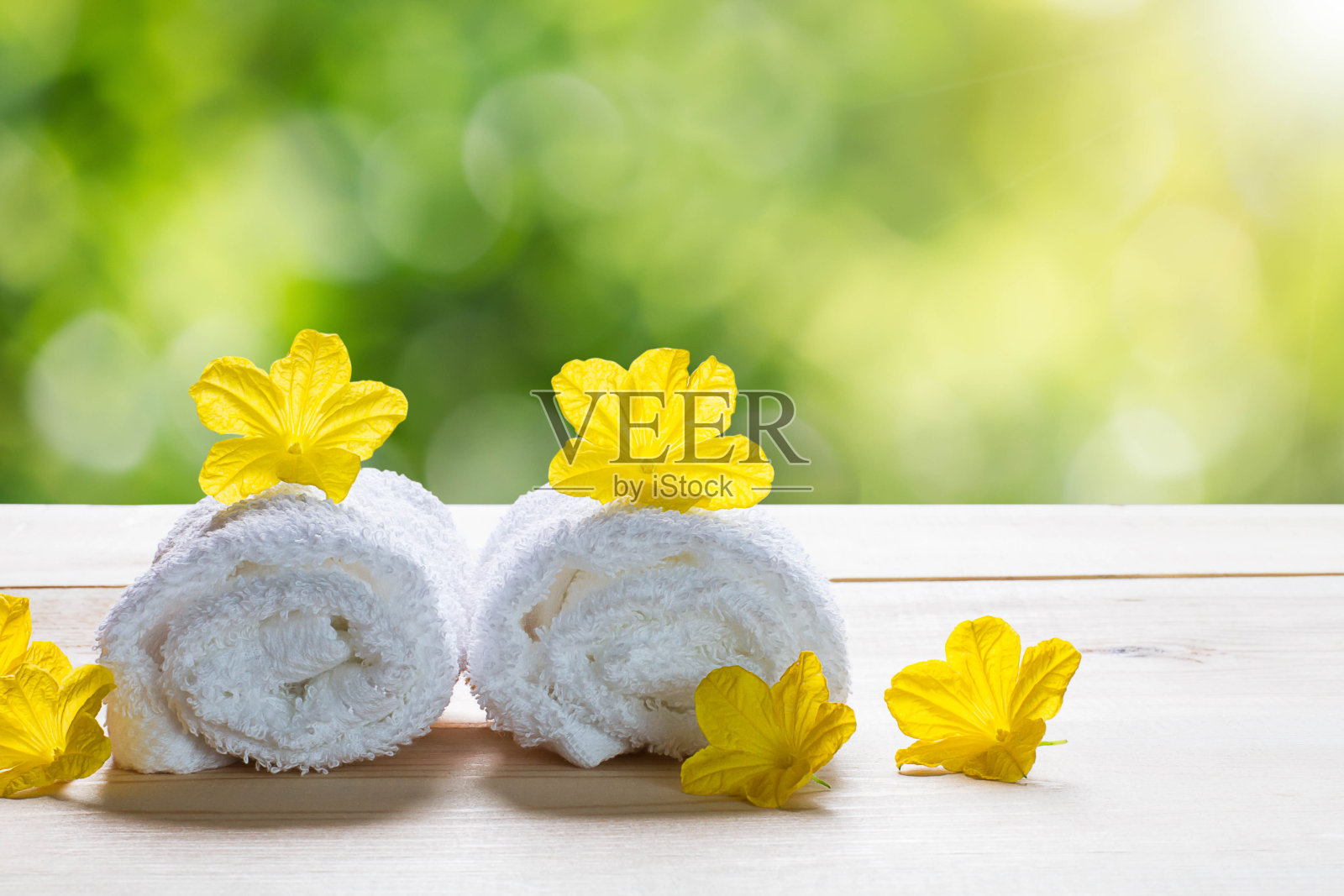 白色毛巾与黄色花朵木地板模糊的绿色散景背景，水疗概念照片摄影图片