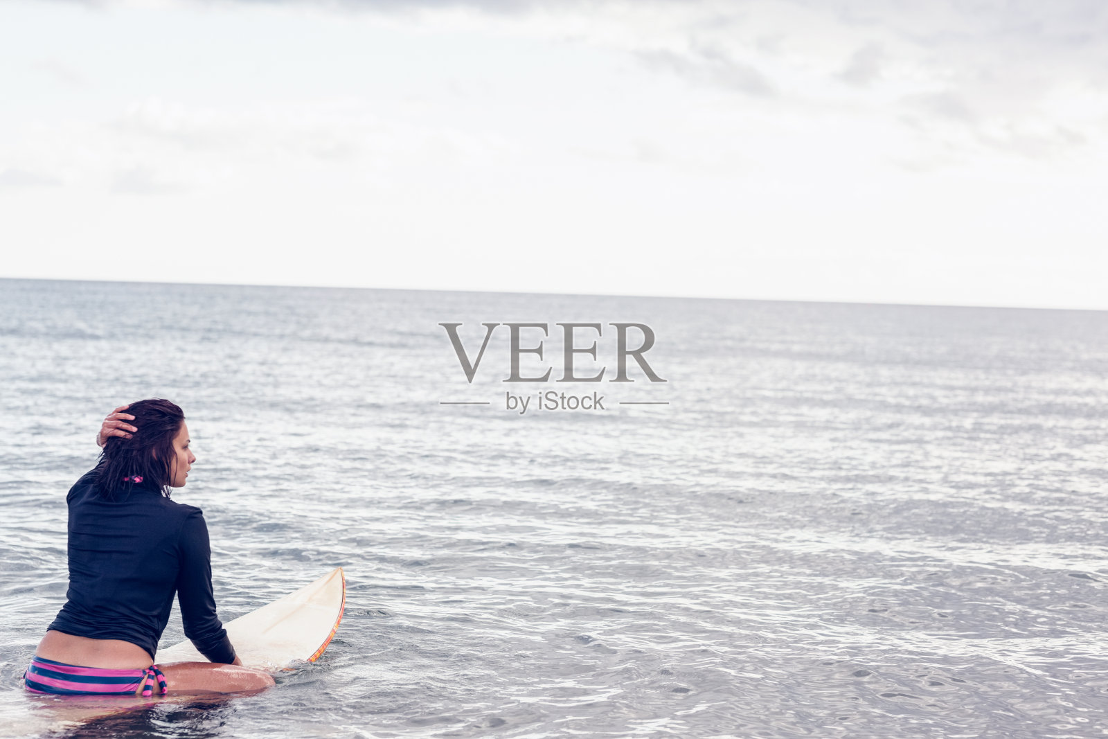 一个女人坐在水里的冲浪板上的后视图照片摄影图片