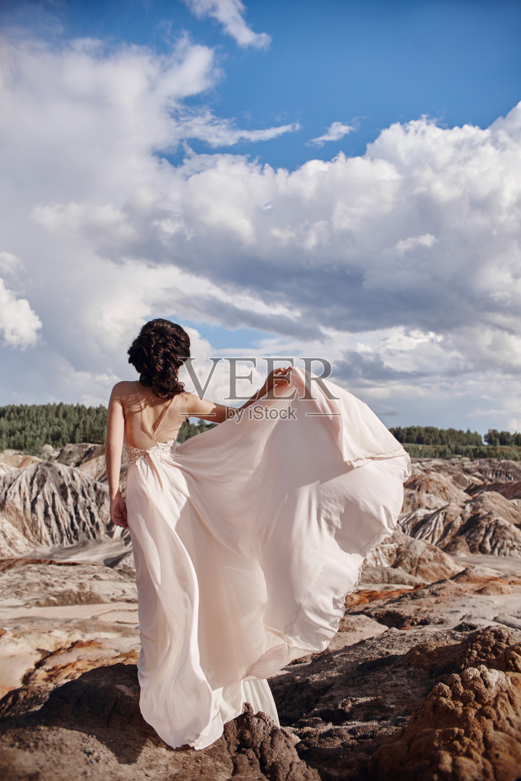 身穿粉红色连衣裙的黑发女郎站在悬崖上，风吹皱了一件连衣裙，一个温柔的女孩形象。令人难以置信的山地景观。风中女人照片摄影图片