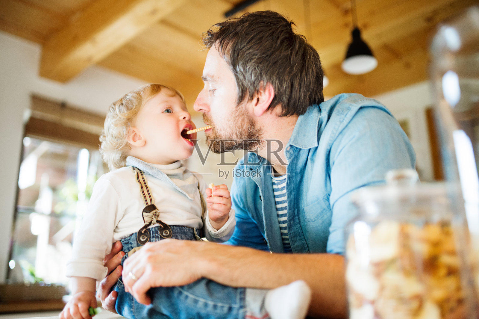 年轻的父亲在家里和他的小儿子一起吃饼干。照片摄影图片