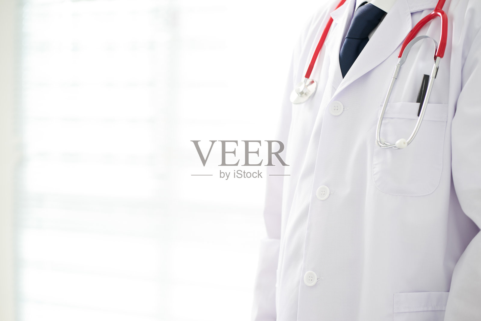 无名医生在办公室摆姿势，他戴着听诊器。照片摄影图片