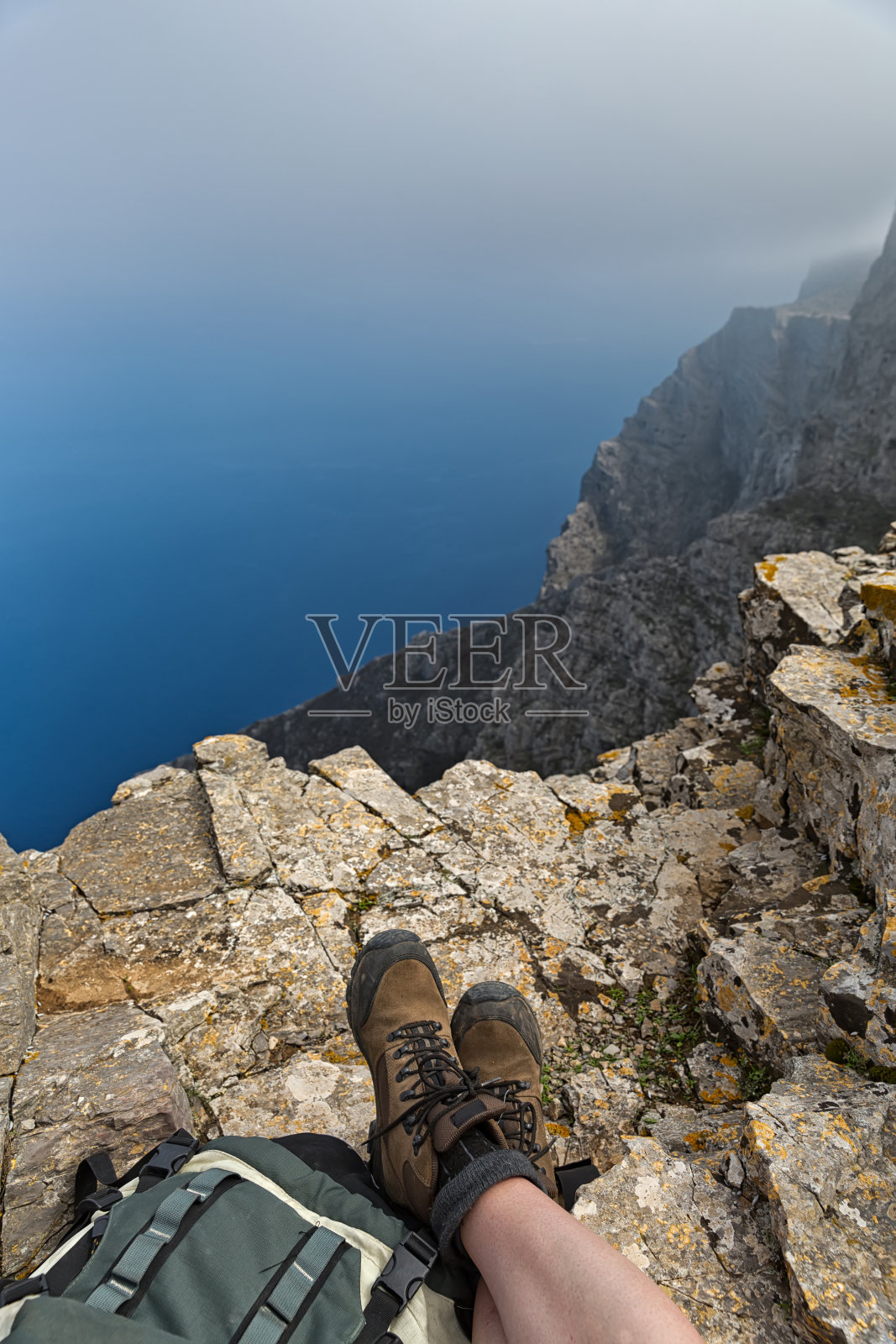 穿着登山靴的女人坐在石头上吃零食，欣赏美丽的海景照片摄影图片