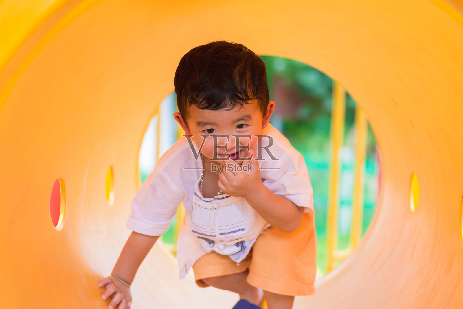 可爱的亚洲男孩玩和微笑在黄色隧道在操场与阳光黄色管，照片摄影图片