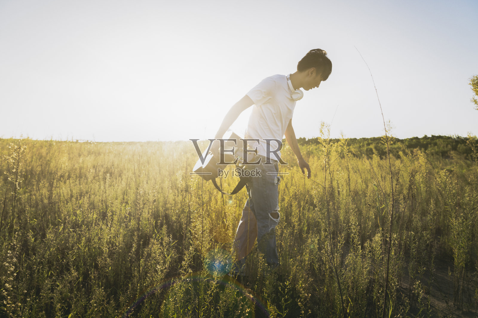 年轻的亚洲人拿着吉他走在田野里照片摄影图片