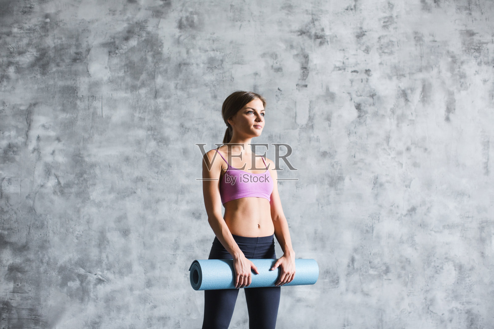 肖像微笑的健身妇女抱着瑜伽垫。照片摄影图片