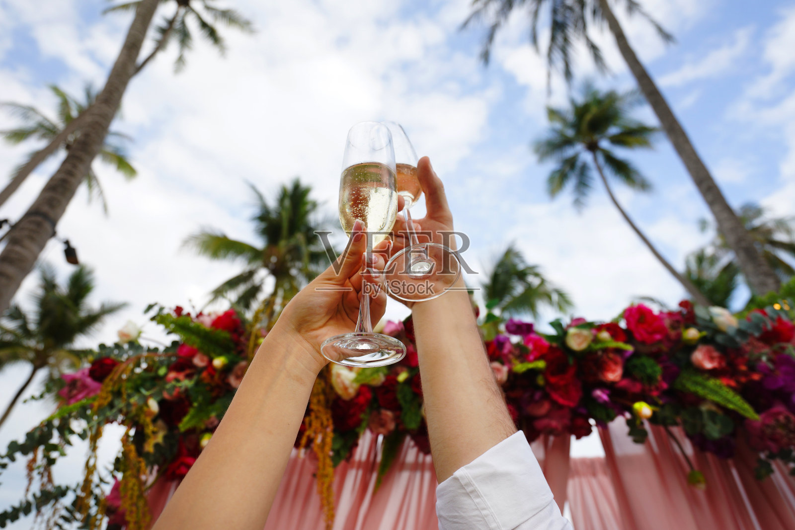 戴眼镜的男人和女人的手高举在婚礼拱门上。照片摄影图片