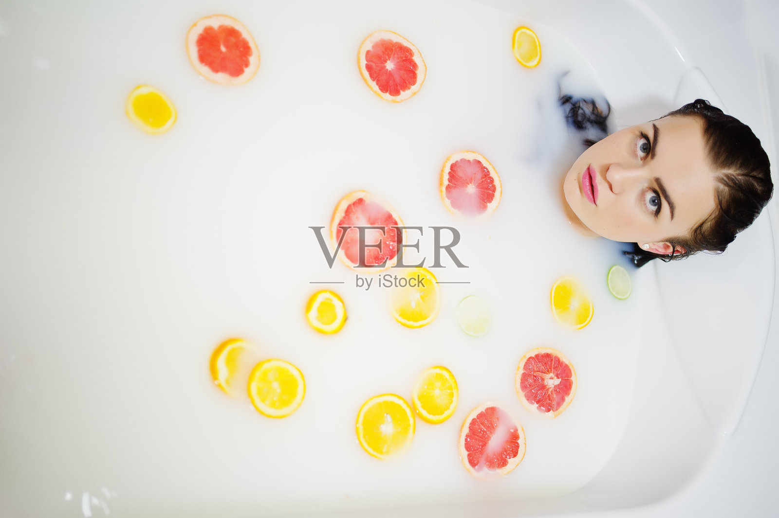 性感的黑发女孩在浴室喝着牛奶和水果。青春沐浴身体。照片摄影图片