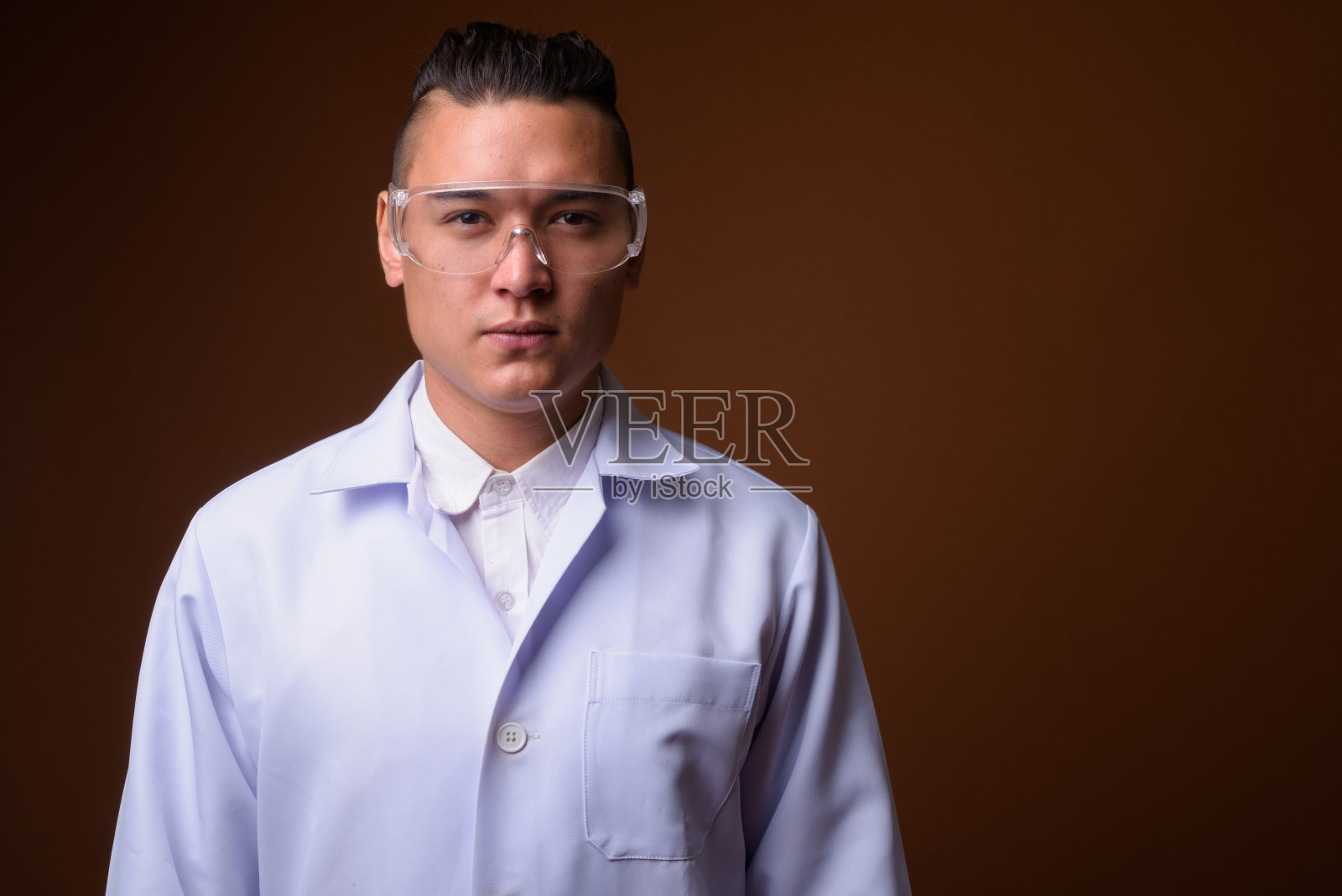 工作室拍摄的年轻英俊的多民族男子医生戴着保护眼镜，以有色背景照片摄影图片