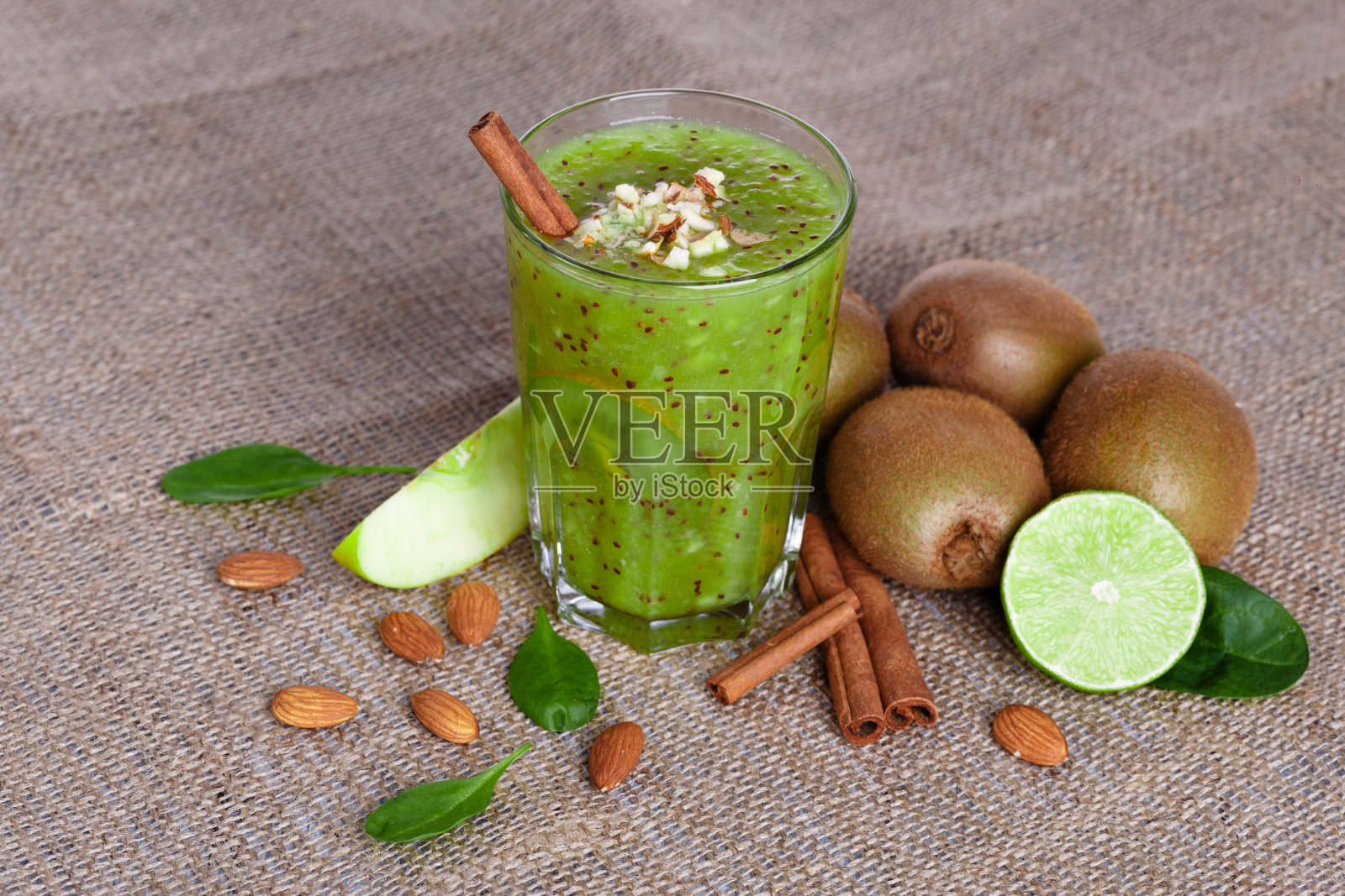 俯视图与猕猴桃，酸橙和苹果在浅棕色的织物背景上的健康饮料。桌上有肉桂，杏仁。照片摄影图片