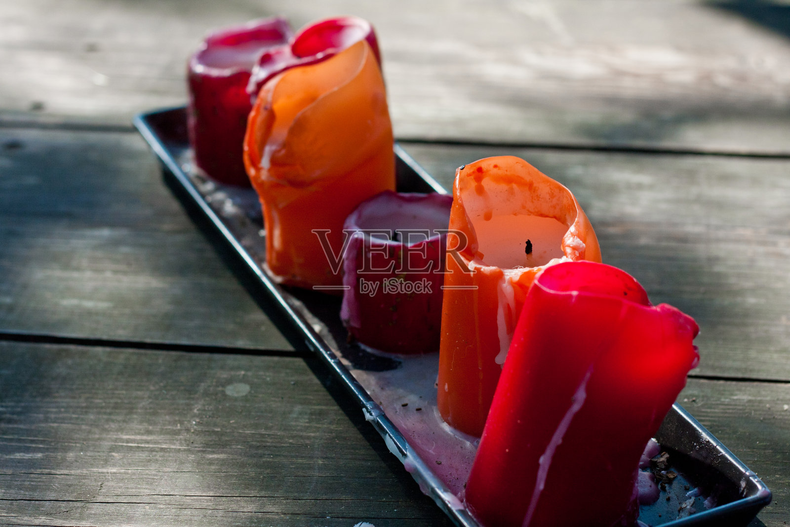 几支五颜六色的大蜡烛放在一个陶瓷支架上，放在一个古老的乡村桌子上，在阳光的照射下，人工蜡烛照明，花园装饰照片摄影图片