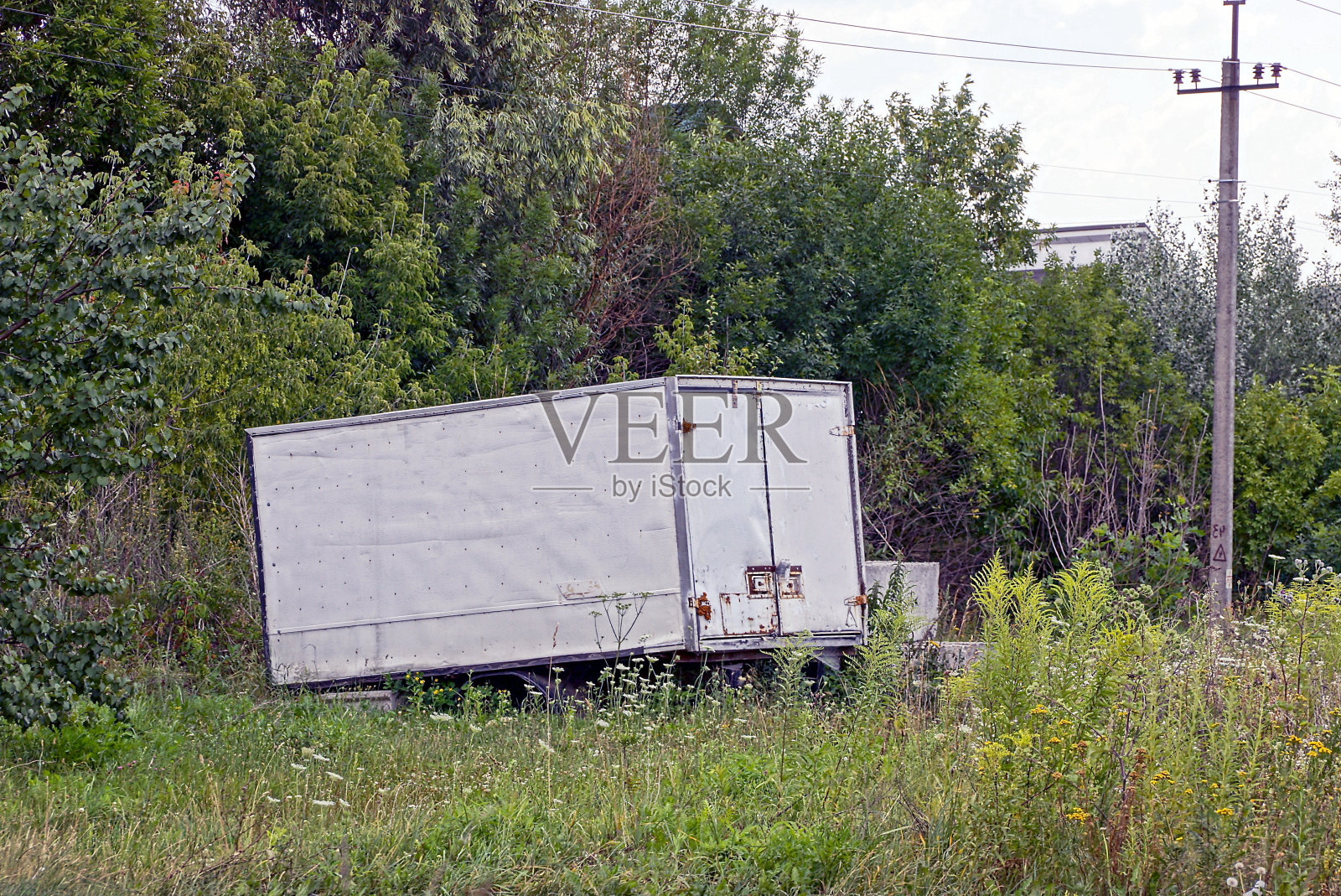 一个灰色的铁容器立在树旁的草地上照片摄影图片