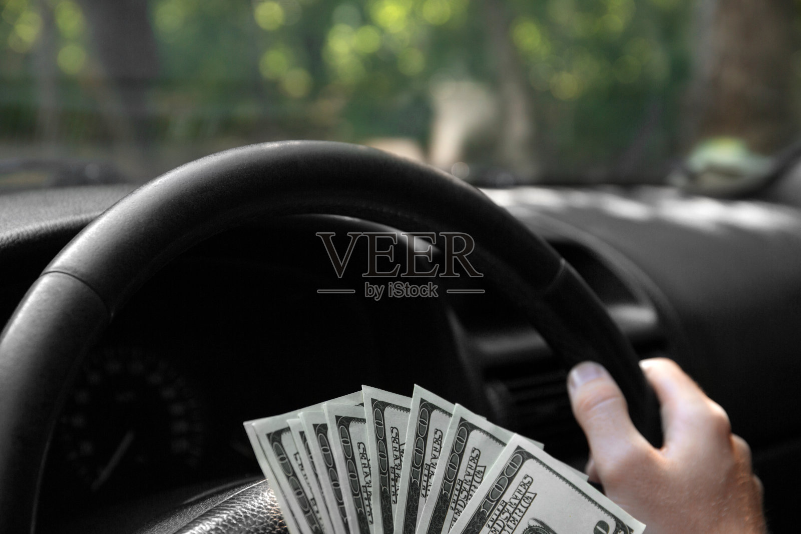 车轮上的美元特写。一个男人的手拿着钱，背景是一辆黑色的车。投资的概念。副本的空间。照片摄影图片