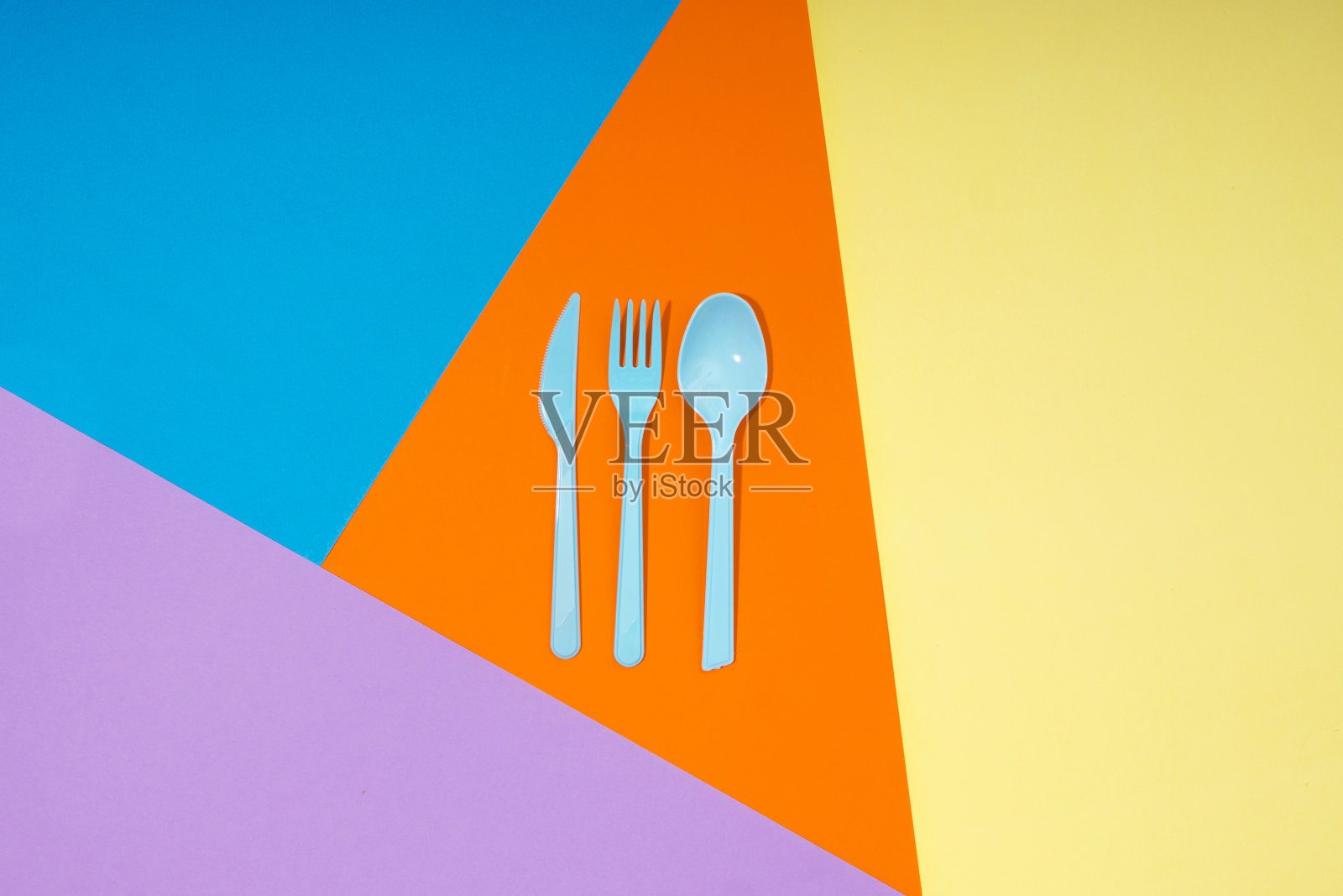 勺子，刀，叉在橙色，黄色，紫色和蓝色的纸张背景照片摄影图片