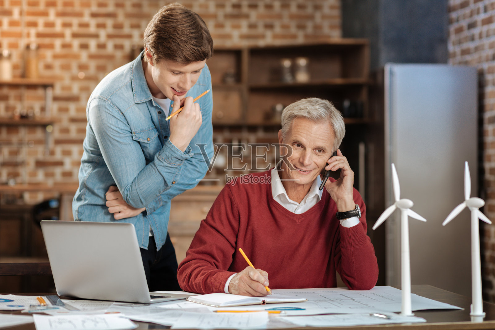一个年轻人偷看他的同事打电话给某人的笔记本照片摄影图片