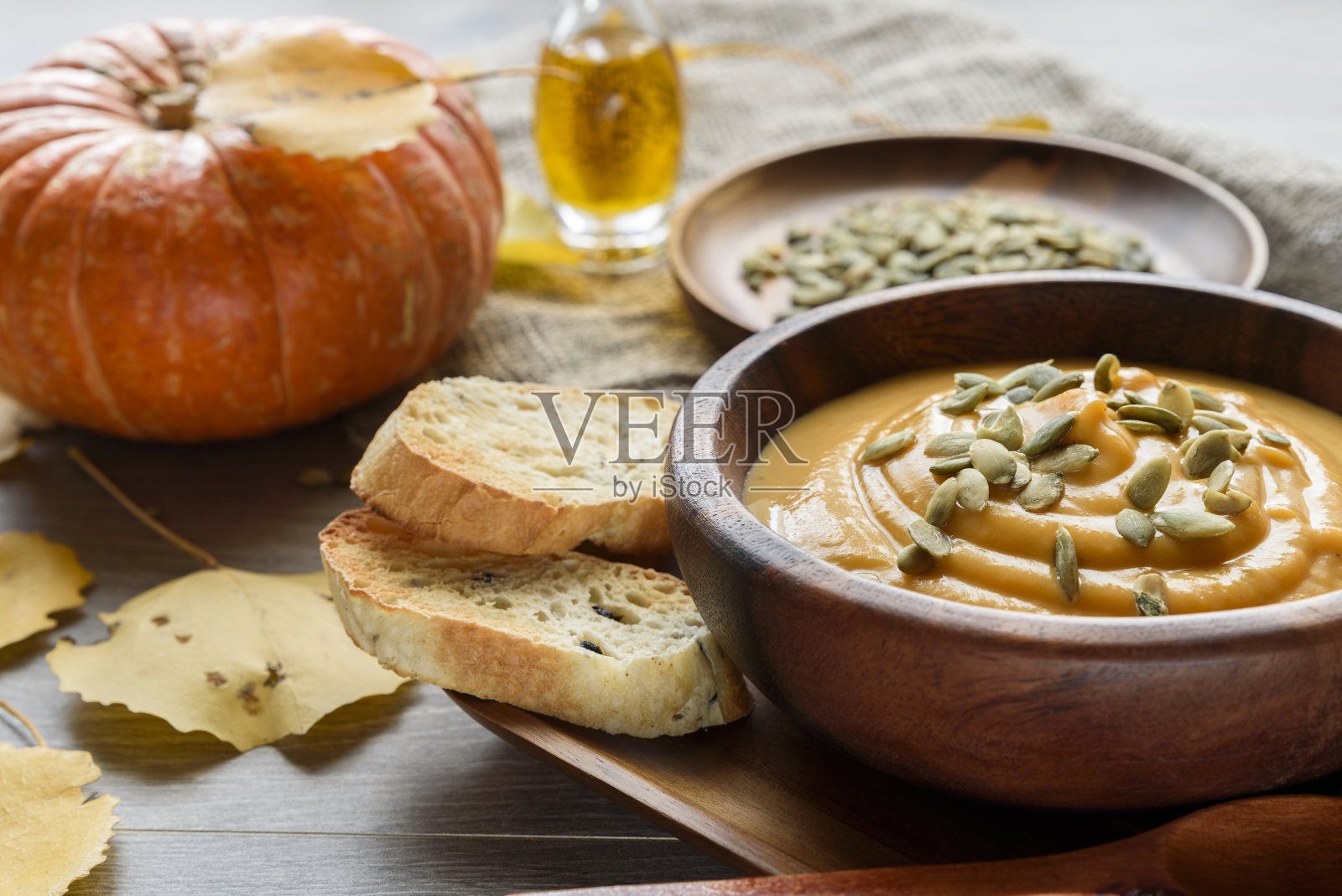 南瓜汤装在木碗里，配上秋叶和南瓜照片摄影图片