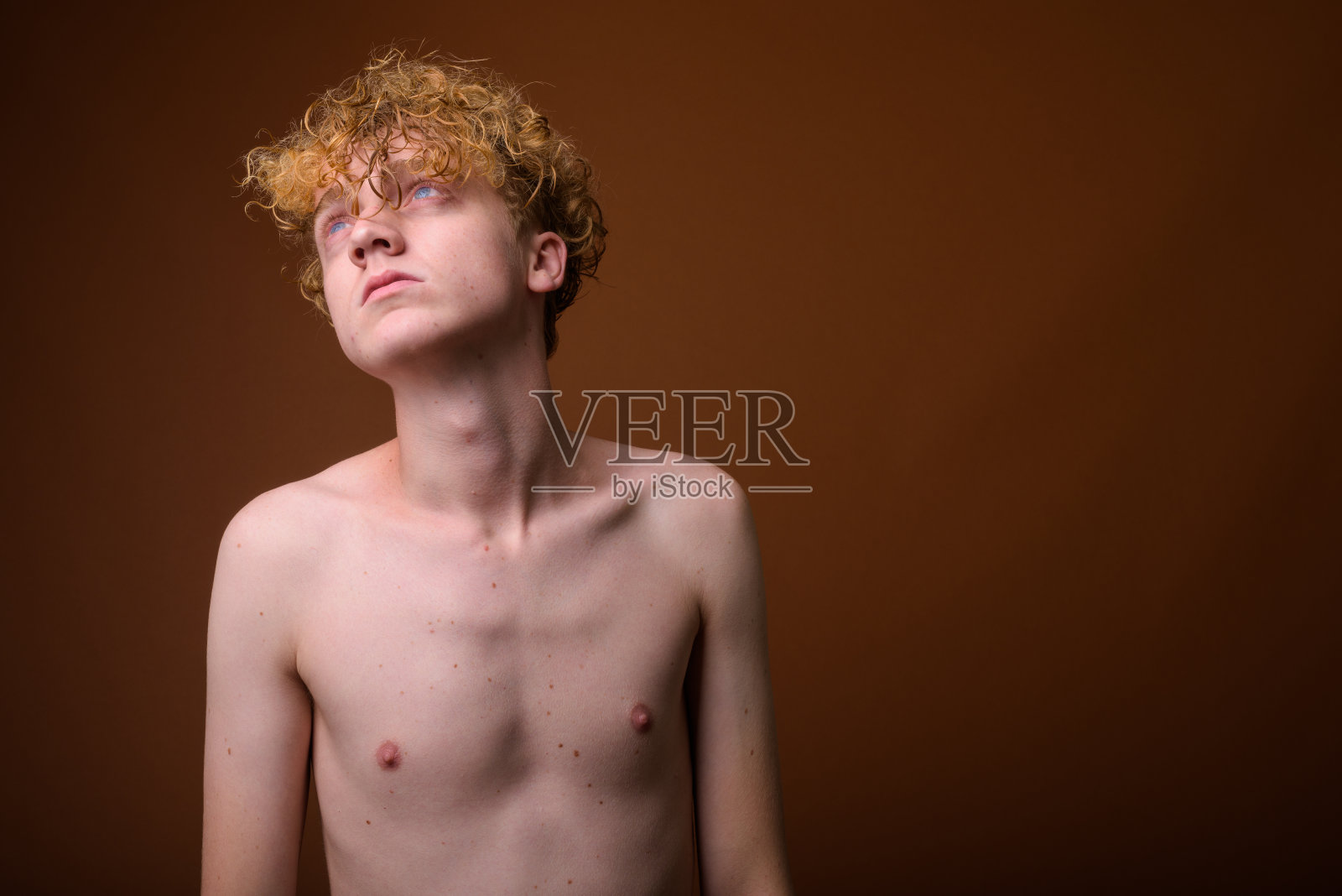 摄影棚拍摄的年轻男子一头金色卷发，上身赤裸，背景是彩色的照片摄影图片