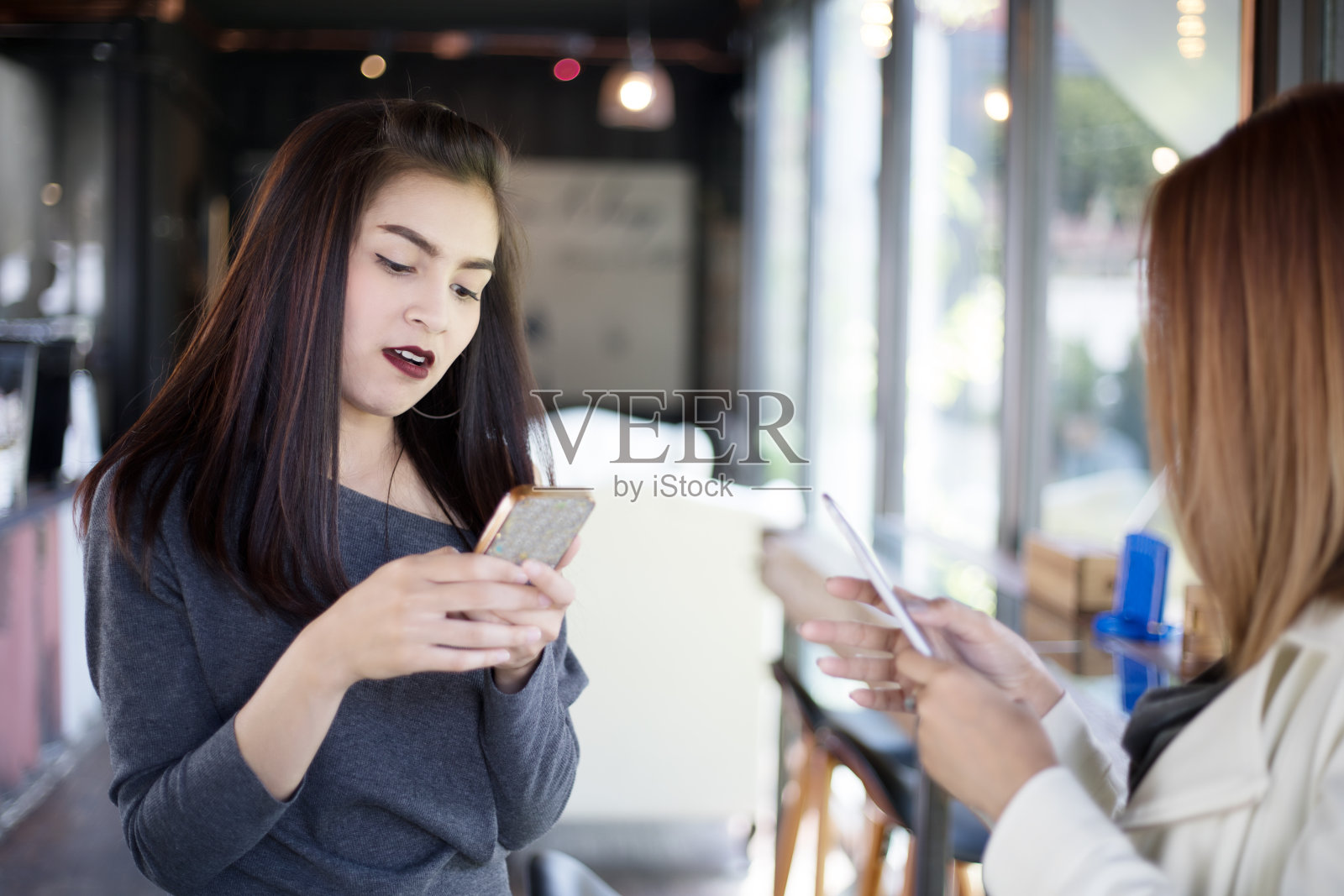 年轻女孩坐在办公室客厅里看着朋友的手机，感到兴奋和微笑照片摄影图片