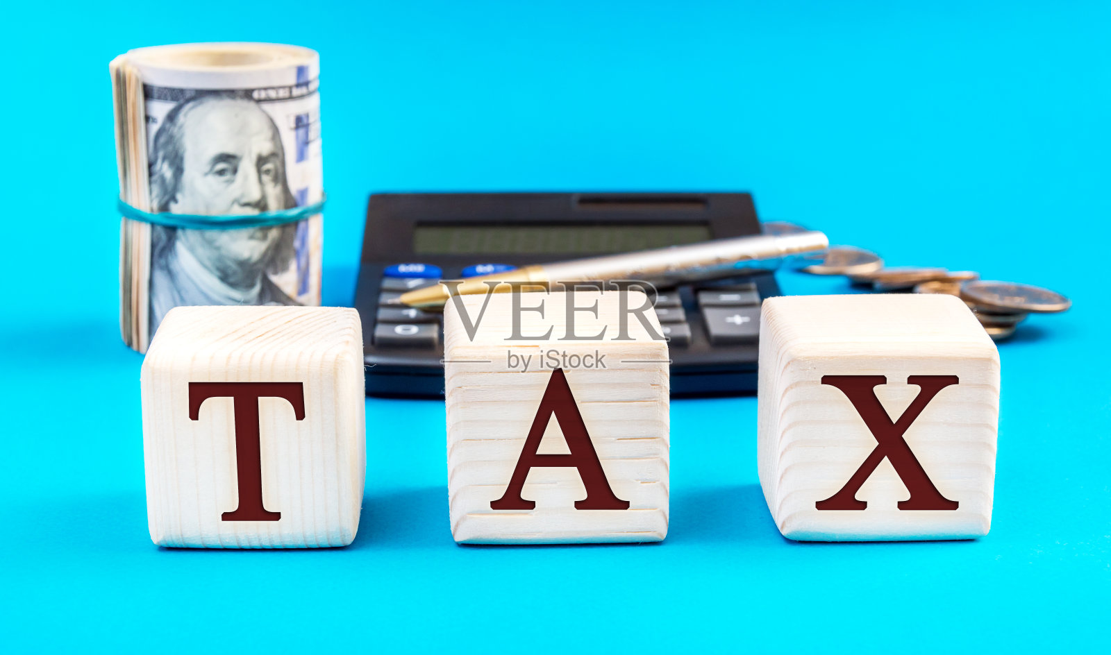 单词“TAX”写的木方与钱，钢笔和计算器在蓝色。经营理念。照片摄影图片
