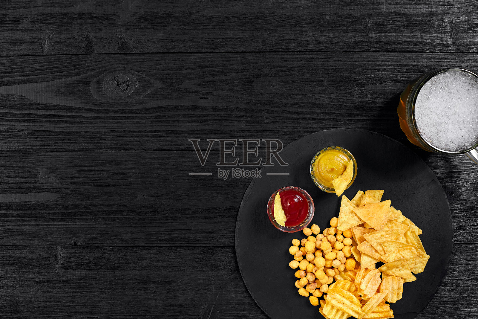 黑色木桌上的啤酒杯和小吃及酱汁的俯视图照片摄影图片
