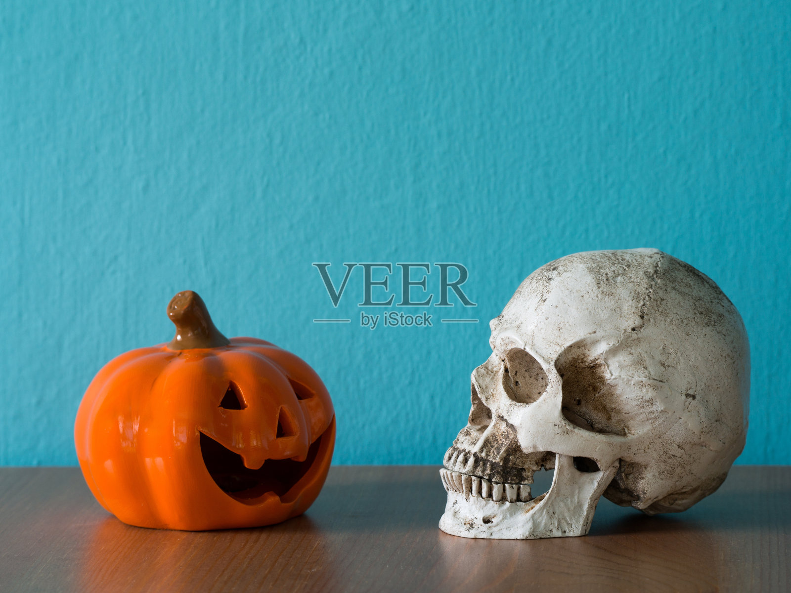 骷髅头和万圣节南瓜帽放在木桌上。背景是蓝色和文本复制空间照片摄影图片